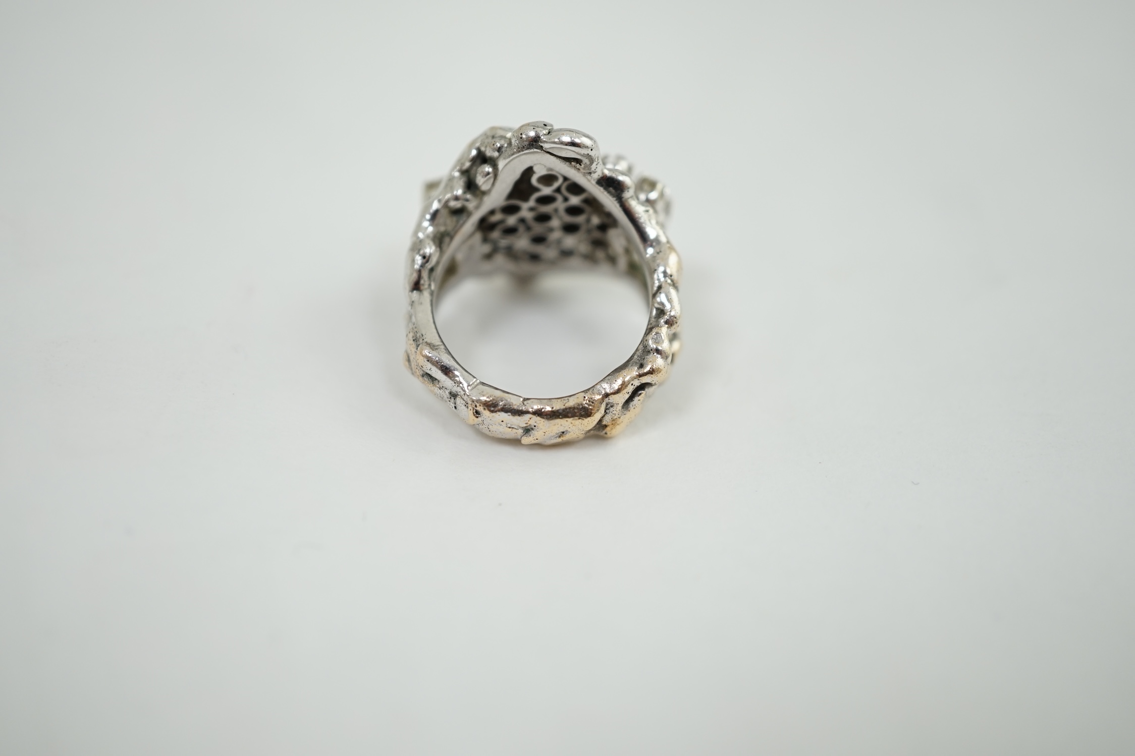 A modernist cast unmarked white metal dress ring, claw set with twenty small diamonds